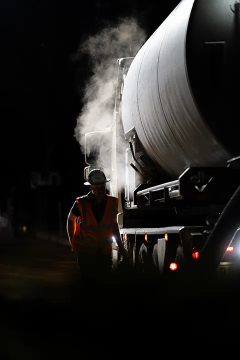 Medewerker bij een betontransportwagen tijdens nachtelijke werkzaamheden.